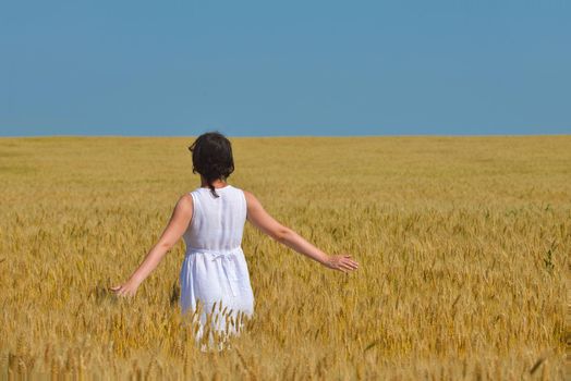 Young woman standing jumping and running  on a wheat field with blue sky in  background at summer day representing healthy life and agriculture concept