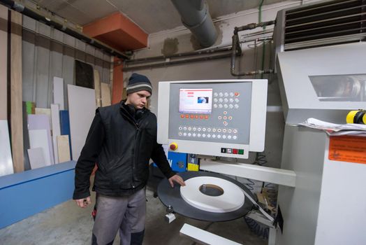 young carpenter calculating and programming a cnc wood working machine in workshop. wood worker preparing a computer program for CNC machine at big modern carpentry