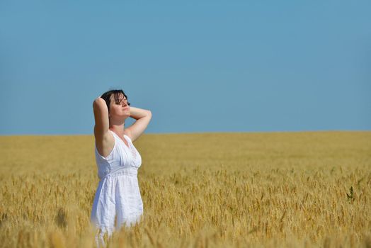 Young woman standing jumping and running  on a wheat field with blue sky in  background at summer day representing healthy life and agriculture concept