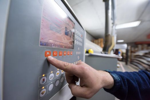 young carpenter calculating and programming a cnc wood working machine in workshop. wood worker preparing a computer program for CNC machine at big modern carpentry