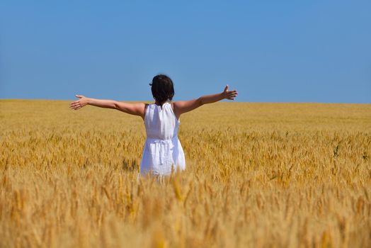 Young woman standing jumping and running  on a wheat field with blue sky the background at summer day representing healthy life and agriculture concept