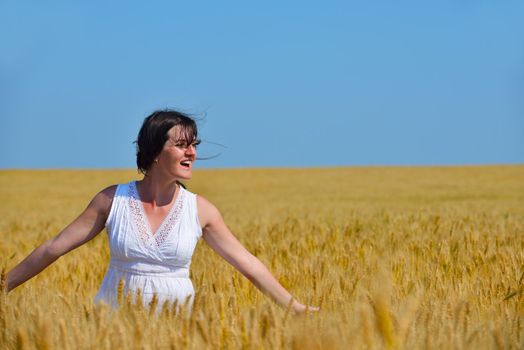 Young woman standing jumping and running  on a wheat field with blue sky the background at summer day representing healthy life and agriculture concept