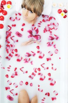 woman beauty spa and wellness treathment with red flower petals in bath with milk 