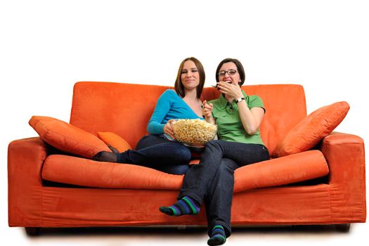 female friends eating popcorn and watching tv at home on orange sofa isolated on white