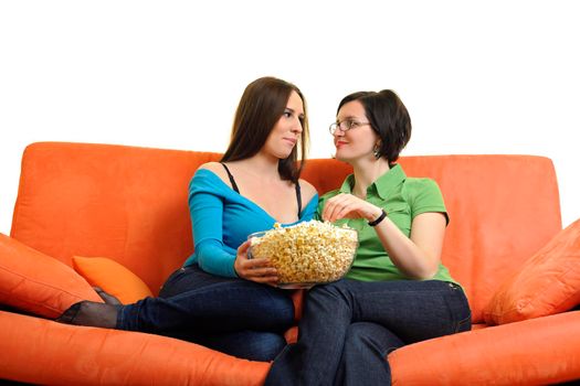 female friends eating popcorn and watching tv at home on orange sofa isolated on white