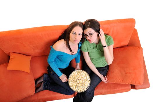 female friends eating popcorn and watching tv at home on orange sofa isolated on white