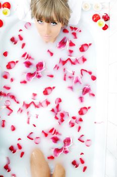 woman beauty spa and wellness treathment with red flower petals in bath with milk 