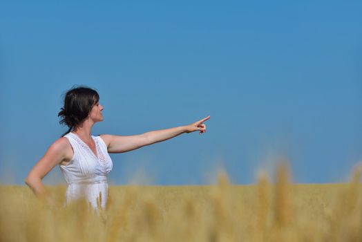 Young woman standing jumping and running  on a wheat field with blue sky in  background at summer day representing healthy life and agriculture concept