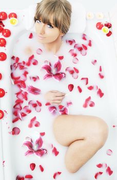 woman beauty spa and wellness treathment with red flower petals in bath with milk 