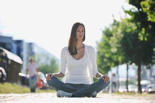 beautiful young woman meditating and exercise yoga in lotus position at street at beautiful sunny day with blured background