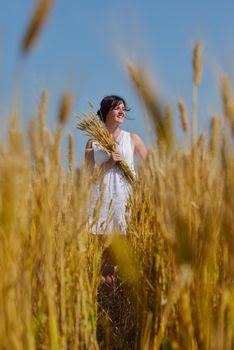 Young woman standing jumping and running  on a wheat field with blue sky in  background at summer day representing healthy life and agriculture concept