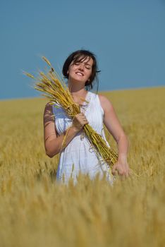 Young woman standing jumping and running  on a wheat field with blue sky in  background at summer day representing healthy life and agriculture concept