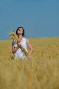 Young woman standing jumping and running  on a wheat field with blue sky in  background at summer day representing healthy life and agriculture concept