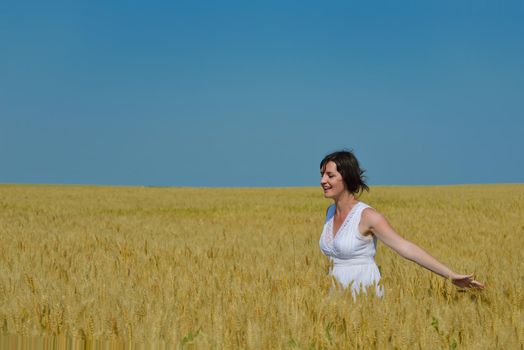Young woman standing jumping and running  on a wheat field with blue sky in  background at summer day representing healthy life and agriculture concept