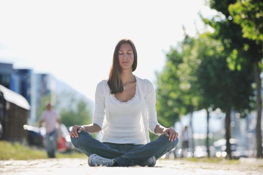 beautiful young woman meditating and exercise yoga in lotus position at street at beautiful sunny day with blured background