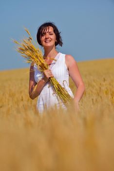 Young woman standing jumping and running  on a wheat field with blue sky the background at summer day representing healthy life and agriculture concept