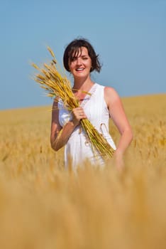 Young woman standing jumping and running  on a wheat field with blue sky the background at summer day representing healthy life and agriculture concept