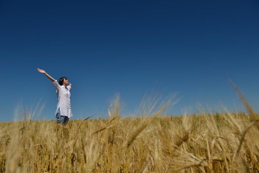 Young woman standing jumping and running  on a wheat field with blue sky in  background at summer day representing healthy life and agriculture concept