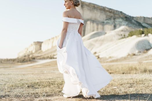 Back view of a beautiful bride in a white dress with bare shoulders standing in a field