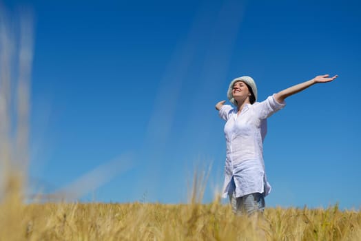 Young woman standing jumping and running  on a wheat field with blue sky in  background at summer day representing healthy life and agriculture concept