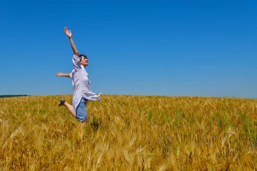 Young woman standing jumping and running  on a wheat field with blue sky the background at summer day representing healthy life and agriculture concept