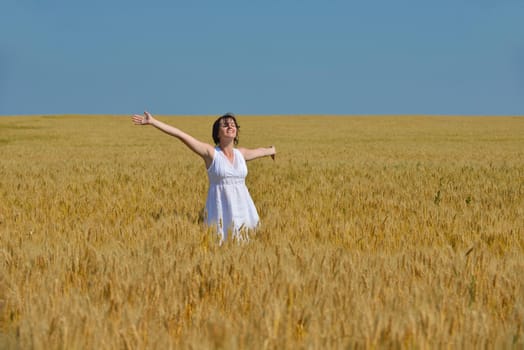 Young woman standing jumping and running  on a wheat field with blue sky in  background at summer day representing healthy life and agriculture concept
