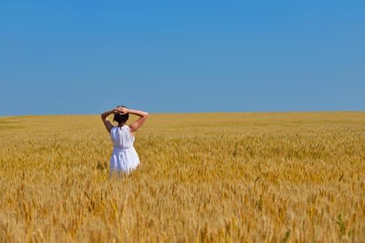 Young woman standing jumping and running  on a wheat field with blue sky the background at summer day representing healthy life and agriculture concept