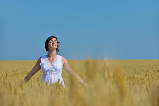Young woman standing jumping and running  on a wheat field with blue sky in  background at summer day representing healthy life and agriculture concept