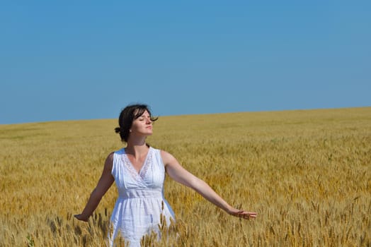 Young woman standing jumping and running  on a wheat field with blue sky in  background at summer day representing healthy life and agriculture concept