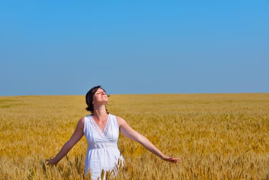 Young woman standing jumping and running  on a wheat field with blue sky the background at summer day representing healthy life and agriculture concept