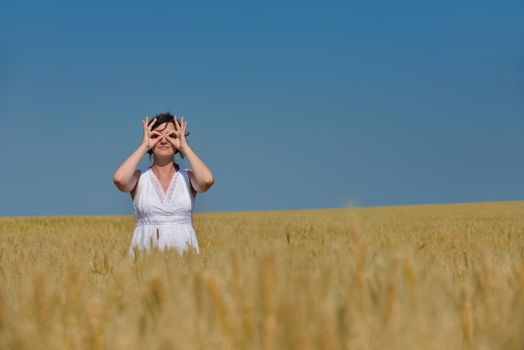 Young woman standing jumping and running  on a wheat field with blue sky in  background at summer day representing healthy life and agriculture concept