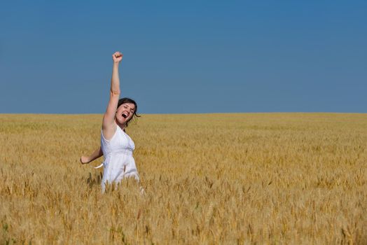 Young woman standing jumping and running  on a wheat field with blue sky in  background at summer day representing healthy life and agriculture concept