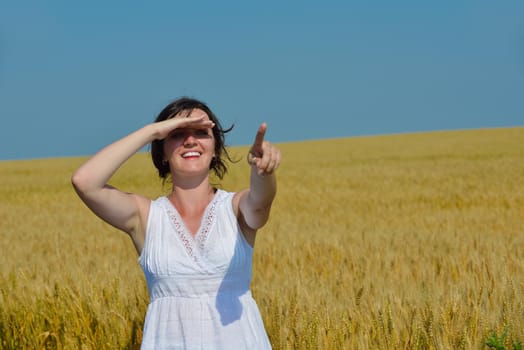 Young woman standing jumping and running  on a wheat field with blue sky in  background at summer day representing healthy life and agriculture concept