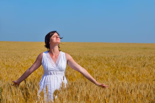 Young woman standing jumping and running  on a wheat field with blue sky the background at summer day representing healthy life and agriculture concept