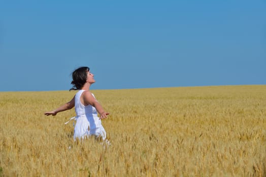 Young woman standing jumping and running  on a wheat field with blue sky in  background at summer day representing healthy life and agriculture concept