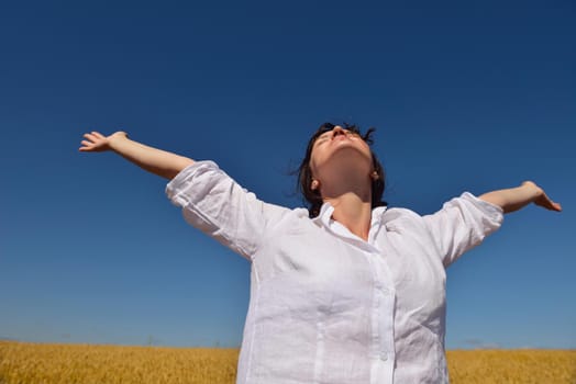 Young woman standing jumping and running  on a wheat field with blue sky the background at summer day representing healthy life and agriculture concept