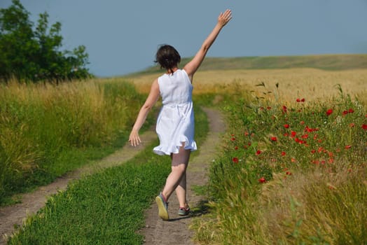 Young woman standing jumping and running  on a wheat field with blue sky in  background at summer day representing healthy life and agriculture concept