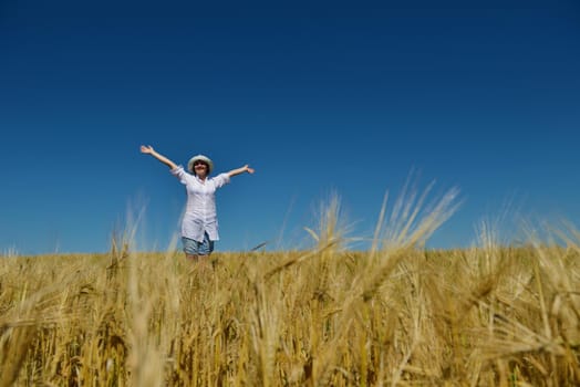 Young woman standing jumping and running  on a wheat field with blue sky in  background at summer day representing healthy life and agriculture concept