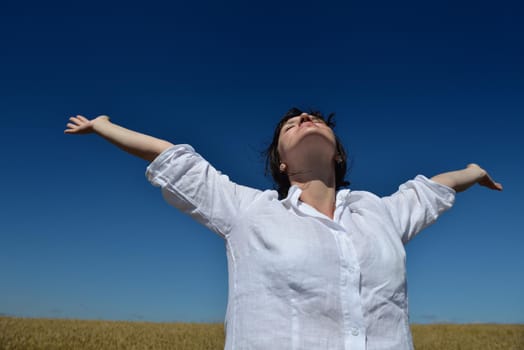 Young woman standing jumping and running  on a wheat field with blue sky the background at summer day representing healthy life and agriculture concept