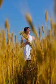 Young woman standing jumping and running  on a wheat field with blue sky the background at summer day representing healthy life and agriculture concept