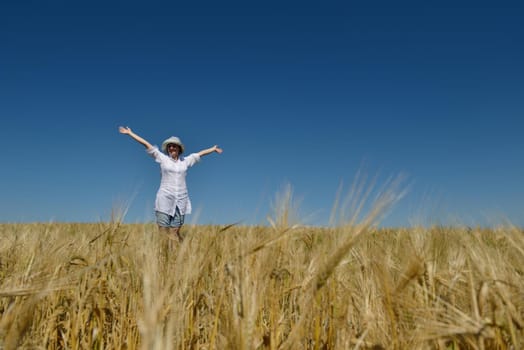 Young woman standing jumping and running  on a wheat field with blue sky the background at summer day representing healthy life and agriculture concept