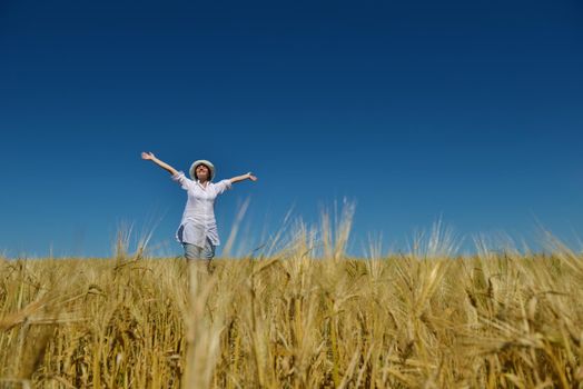 Young woman standing jumping and running  on a wheat field with blue sky in  background at summer day representing healthy life and agriculture concept