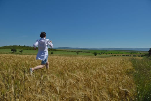 Young woman standing jumping and running  on a wheat field with blue sky in  background at summer day representing healthy life and agriculture concept