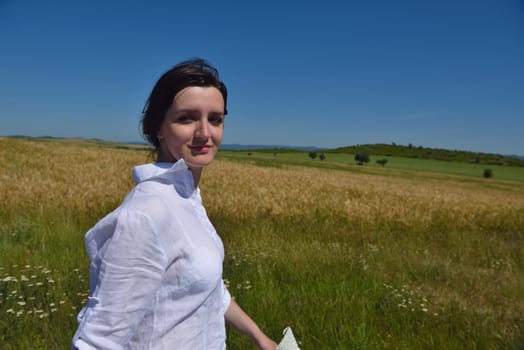 Young woman standing jumping and running  on a wheat field with blue sky in  background at summer day representing healthy life and agriculture concept