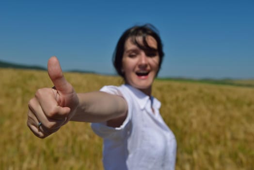 Young woman standing jumping and running  on a wheat field with blue sky in  background at summer day representing healthy life and agriculture concept