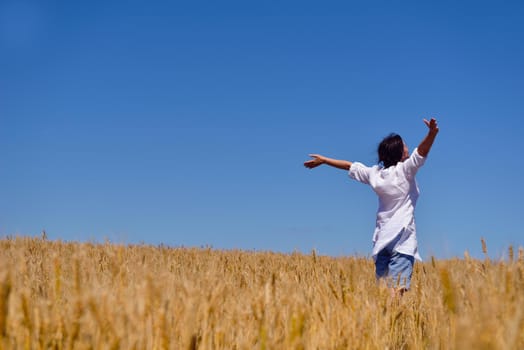 Young woman standing jumping and running  on a wheat field with blue sky the background at summer day representing healthy life and agriculture concept