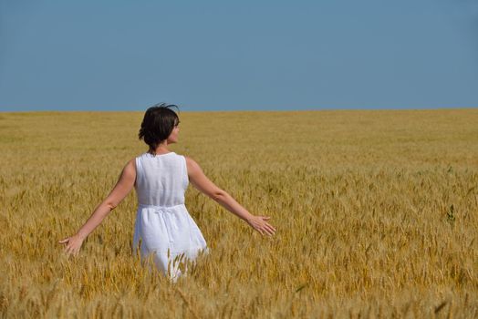 Young woman standing jumping and running  on a wheat field with blue sky the background at summer day representing healthy life and agriculture concept