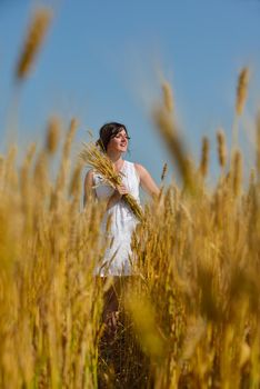 Young woman standing jumping and running  on a wheat field with blue sky the background at summer day representing healthy life and agriculture concept