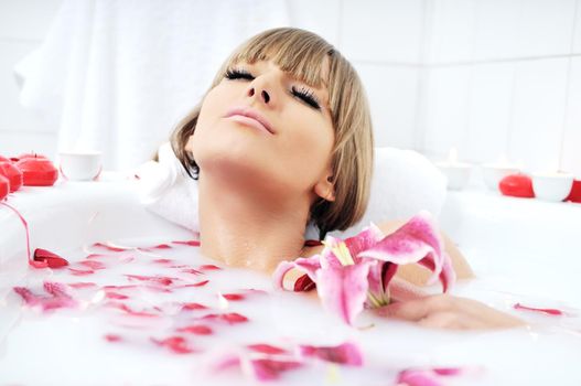 woman beauty spa and wellness treathment with red flower petals in bath with milk 