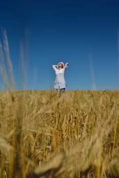 Young woman standing jumping and running  on a wheat field with blue sky the background at summer day representing healthy life and agriculture concept